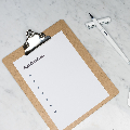 clip board laying flat on a marble countertop, a sheet of paper titled Application is attached to the clipboard. A white pen rests on its top beside. 
